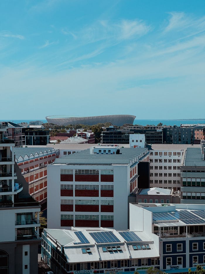 Aerial view of modern Cape Town buildings with ocean and Cape Town Stadium in the background.