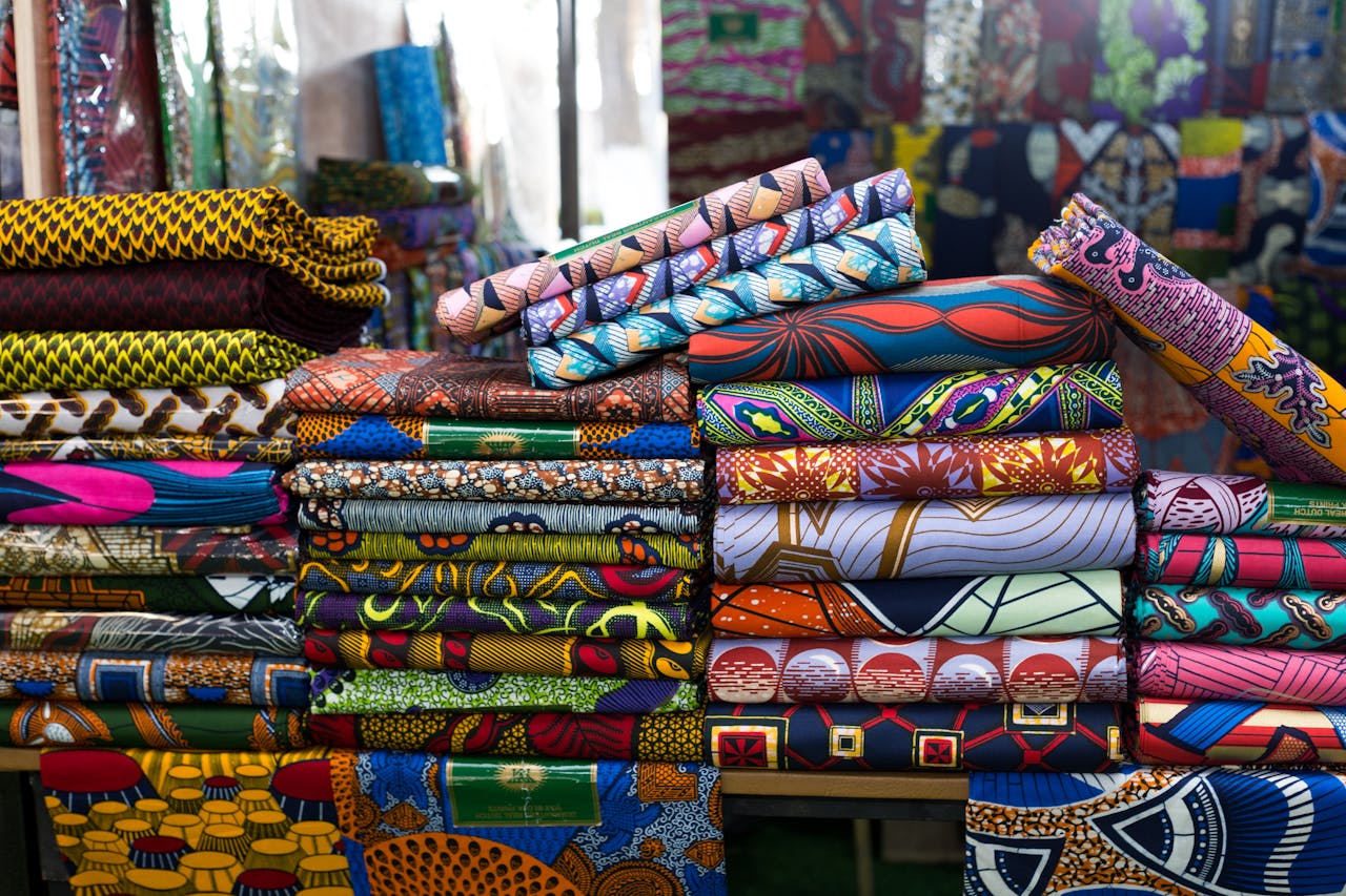 Vibrant stack of African fabrics at a market in Cotonou, showcasing bold patterns and colors.